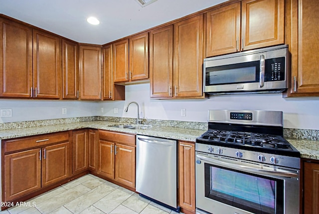 kitchen with light tile patterned floors, stainless steel appliances, light stone countertops, and sink