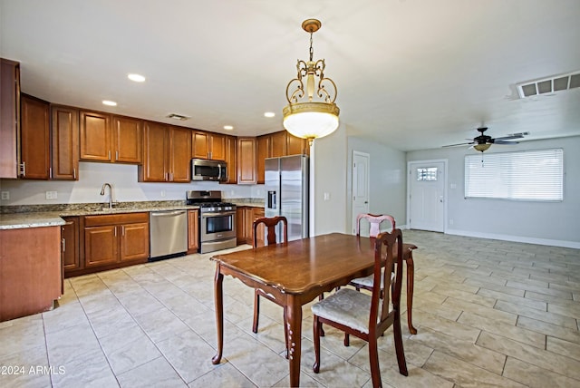 kitchen with appliances with stainless steel finishes, light stone counters, decorative light fixtures, and ceiling fan with notable chandelier