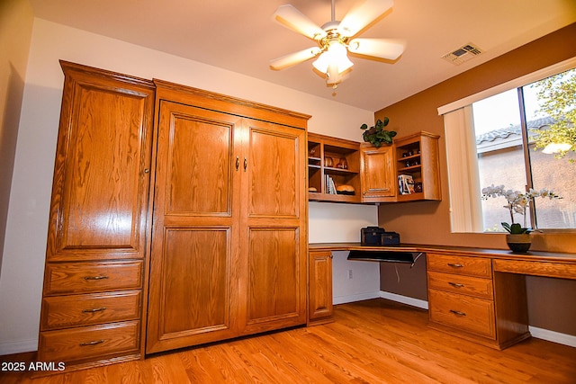 unfurnished office with a ceiling fan, light wood-type flooring, visible vents, and built in desk