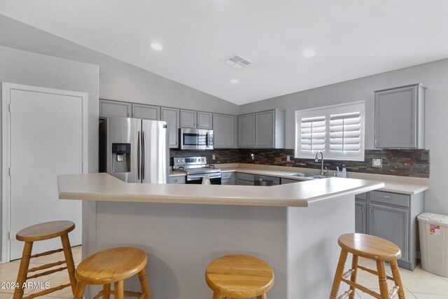 kitchen featuring lofted ceiling, a kitchen breakfast bar, sink, light tile patterned flooring, and appliances with stainless steel finishes