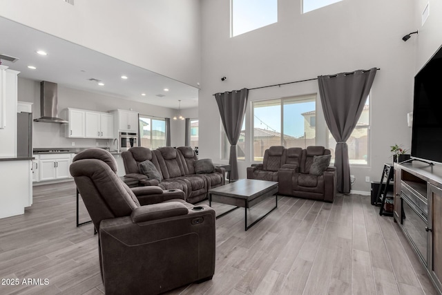 living area featuring a high ceiling, recessed lighting, light wood-type flooring, and a wealth of natural light