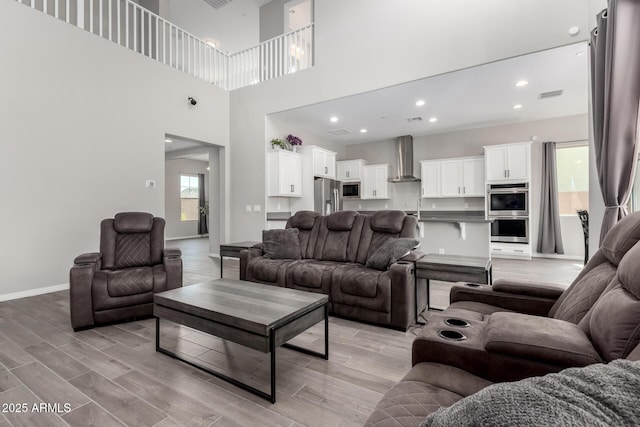 living area featuring visible vents, baseboards, recessed lighting, light wood-style flooring, and a towering ceiling