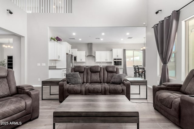 living area featuring light wood-style flooring, baseboards, a towering ceiling, and a chandelier