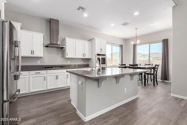 kitchen featuring visible vents, wall chimney exhaust hood, stainless steel fridge with ice dispenser, and gas stovetop