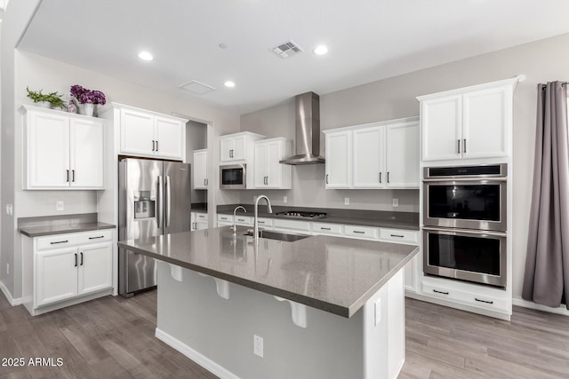 kitchen with stainless steel appliances, light wood-style floors, white cabinets, and wall chimney range hood