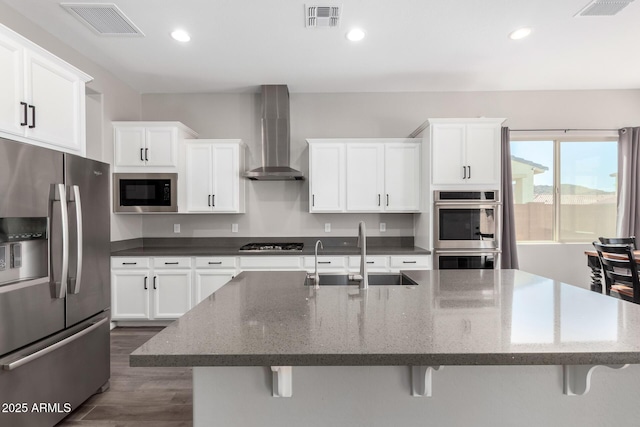 kitchen with visible vents, a sink, stainless steel appliances, a kitchen bar, and wall chimney exhaust hood