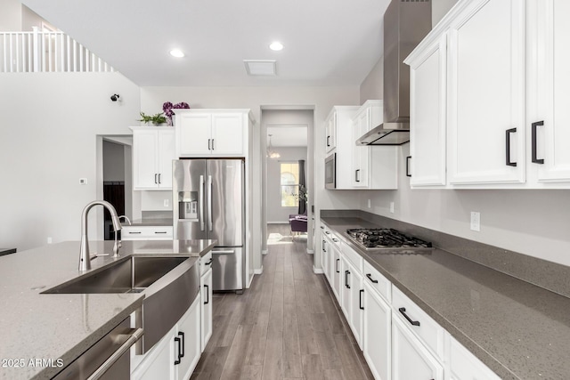 kitchen featuring dark stone countertops, wood finished floors, appliances with stainless steel finishes, white cabinetry, and wall chimney range hood