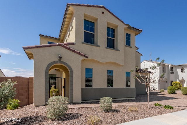 mediterranean / spanish-style house featuring a gate, stucco siding, fence, and a tiled roof