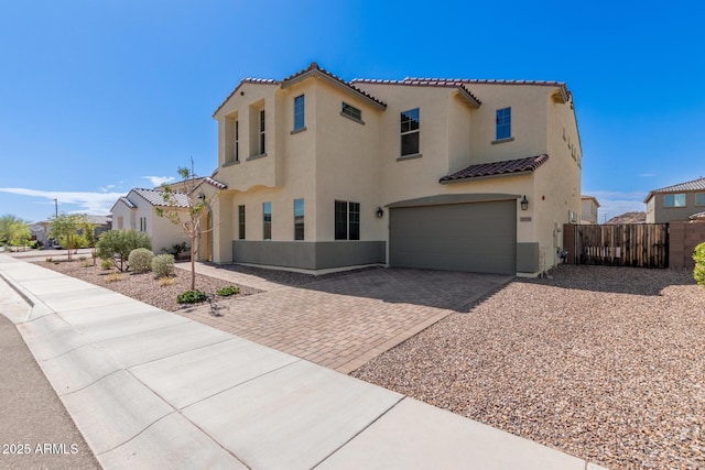 mediterranean / spanish-style home featuring stucco siding, a tile roof, decorative driveway, fence, and an attached garage