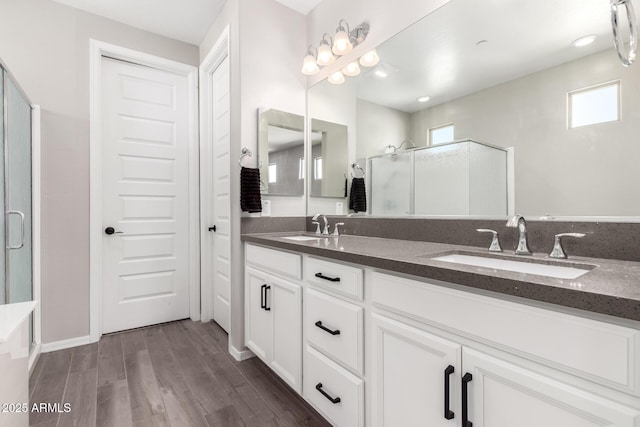 full bathroom featuring double vanity, wood finished floors, a shower with door, and a sink