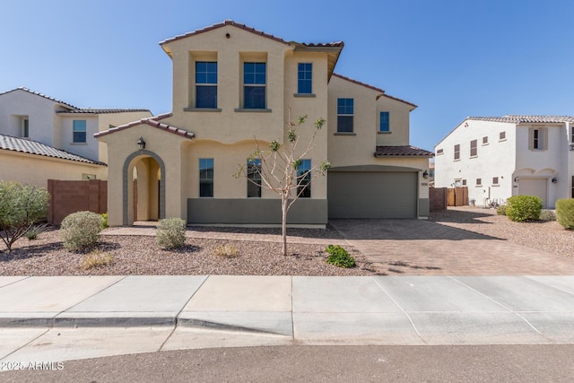 mediterranean / spanish-style home featuring stucco siding, decorative driveway, a garage, and fence