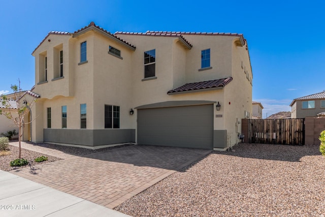 mediterranean / spanish-style home featuring stucco siding, decorative driveway, fence, an attached garage, and a tiled roof