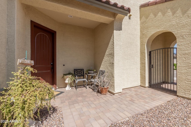 view of exterior entry featuring a gate, stucco siding, a patio area, and a tiled roof