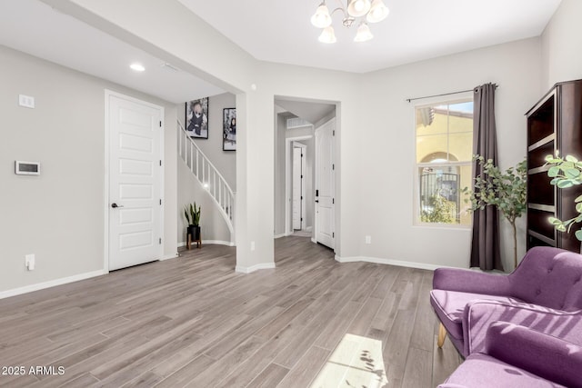 living area featuring stairway, light wood-style flooring, baseboards, and a chandelier