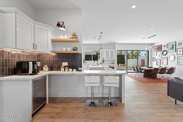 kitchen featuring beverage cooler, light hardwood / wood-style floors, backsplash, white cabinets, and decorative light fixtures