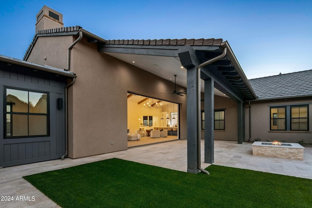 back of property with a lawn, a patio, and an outdoor fire pit