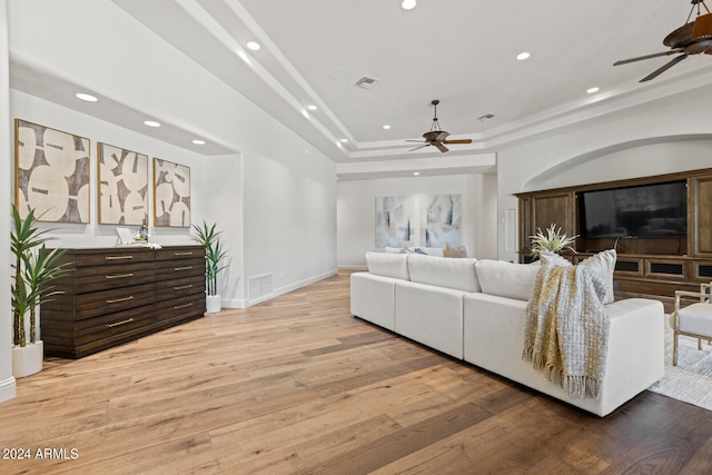 living room featuring hardwood / wood-style floors, ceiling fan, and a tray ceiling