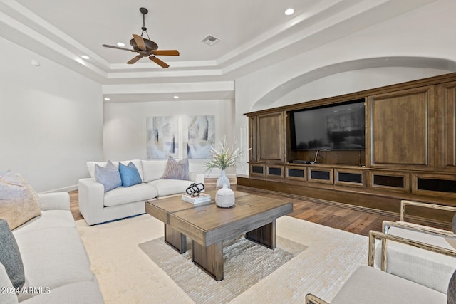 living room with a tray ceiling, ceiling fan, and light hardwood / wood-style flooring