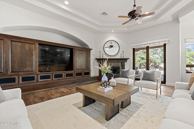 living room with a raised ceiling, ceiling fan, and light wood-type flooring