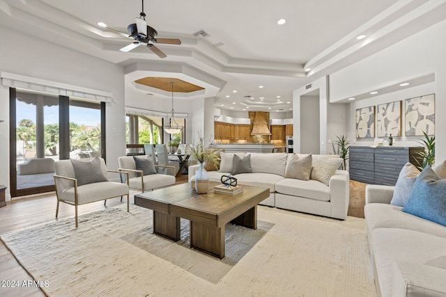 living room with a tray ceiling, ceiling fan, and light hardwood / wood-style floors