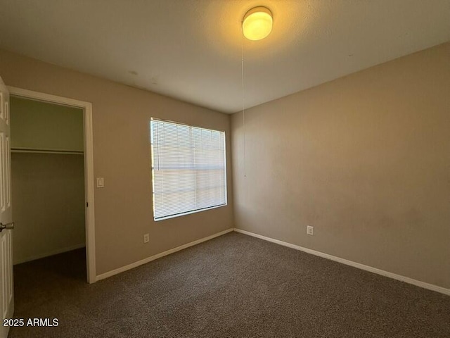 unfurnished bedroom with a spacious closet, a closet, and dark colored carpet