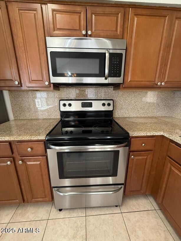 kitchen featuring light stone countertops, decorative backsplash, stainless steel appliances, and light tile patterned flooring