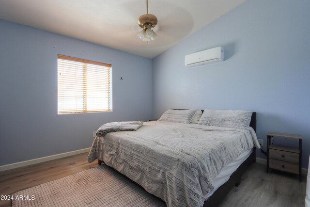 bedroom with a wall mounted air conditioner, hardwood / wood-style flooring, ceiling fan, and lofted ceiling