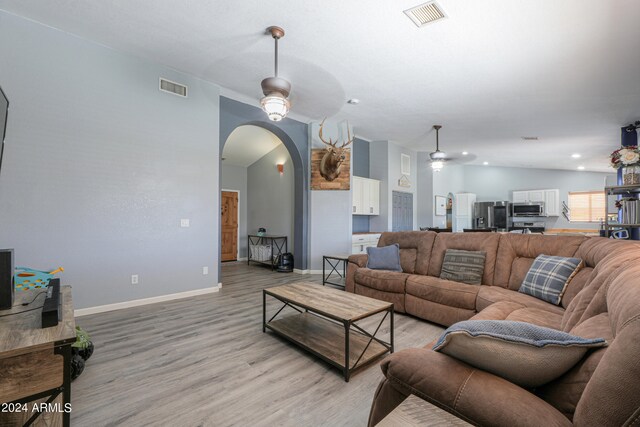 living room with ceiling fan, light hardwood / wood-style floors, and vaulted ceiling