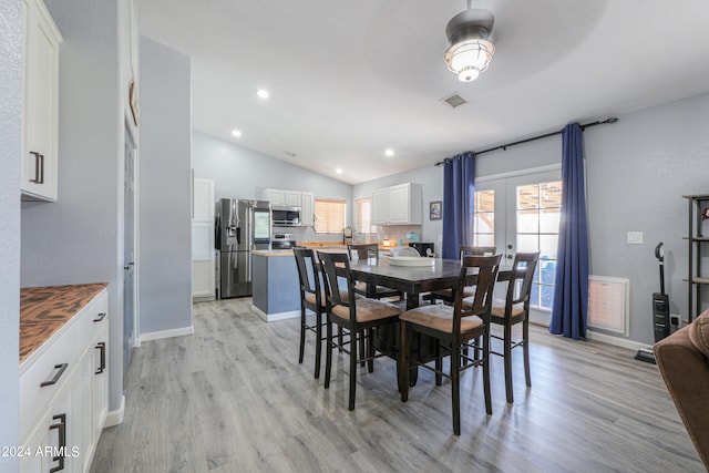 dining space with light hardwood / wood-style floors, french doors, and vaulted ceiling