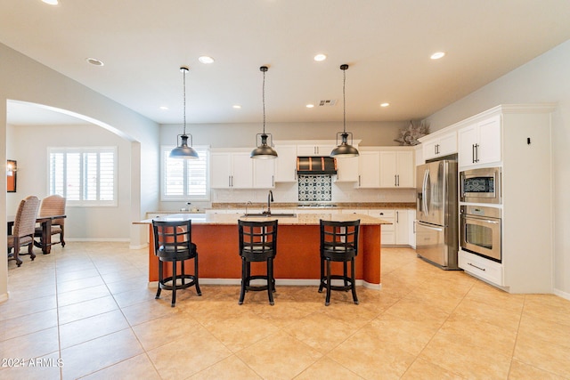 kitchen featuring a center island with sink, appliances with stainless steel finishes, a kitchen bar, and white cabinetry