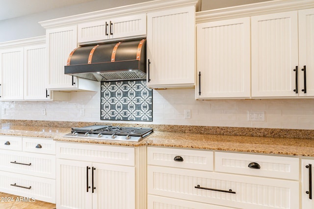 kitchen featuring range hood, backsplash, stainless steel gas stovetop, and light stone counters