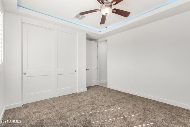 unfurnished bedroom featuring a closet, carpet flooring, ceiling fan, and a raised ceiling