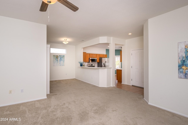 unfurnished living room with a wealth of natural light, light carpet, and ceiling fan