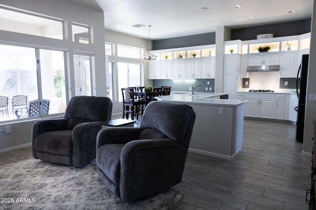 kitchen featuring dark wood-type flooring, gas cooktop, hanging light fixtures, an island with sink, and white cabinets