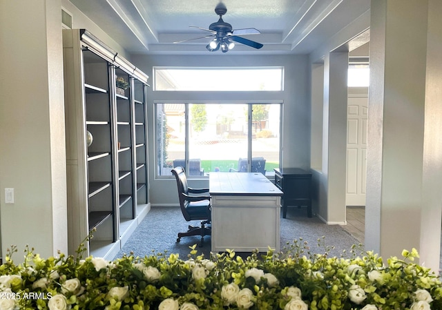 office area featuring light carpet, a raised ceiling, and ceiling fan