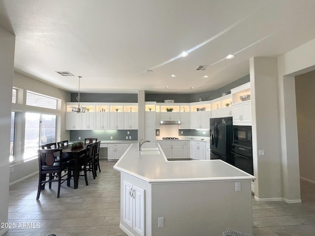 kitchen with white cabinetry, decorative light fixtures, black appliances, and a large island with sink