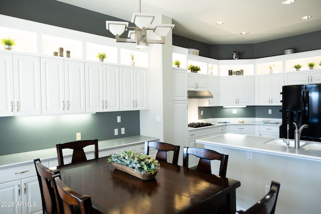 kitchen featuring a breakfast bar, sink, black appliances, hanging light fixtures, and white cabinets