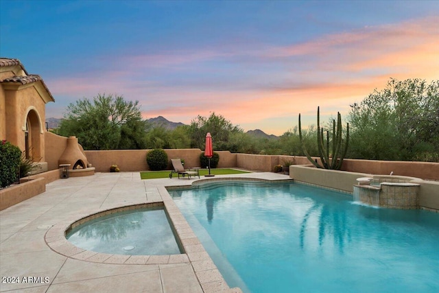 pool at dusk with pool water feature, an in ground hot tub, and a patio