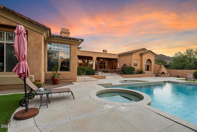 pool at dusk with an in ground hot tub and a patio area