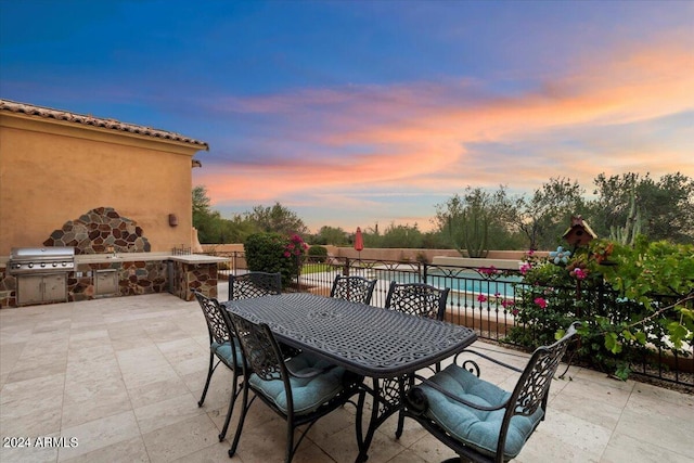 patio terrace at dusk featuring a fenced in pool, area for grilling, and grilling area