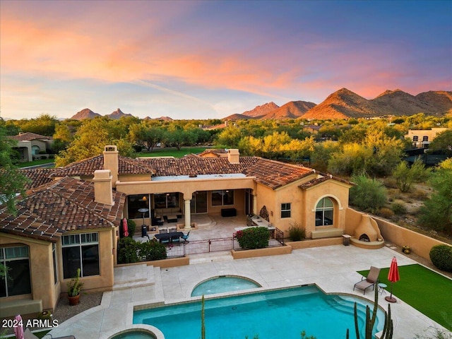 back house at dusk with a mountain view, a patio area, and a swimming pool with hot tub