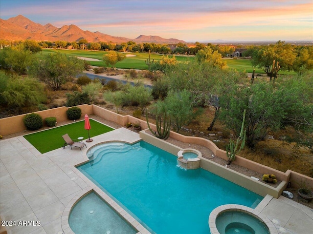 pool at dusk featuring an in ground hot tub, a mountain view, and a patio