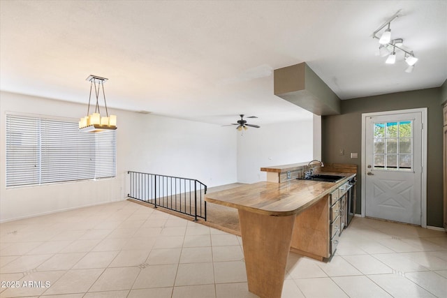 kitchen with a ceiling fan, a sink, a peninsula, light tile patterned floors, and hanging light fixtures