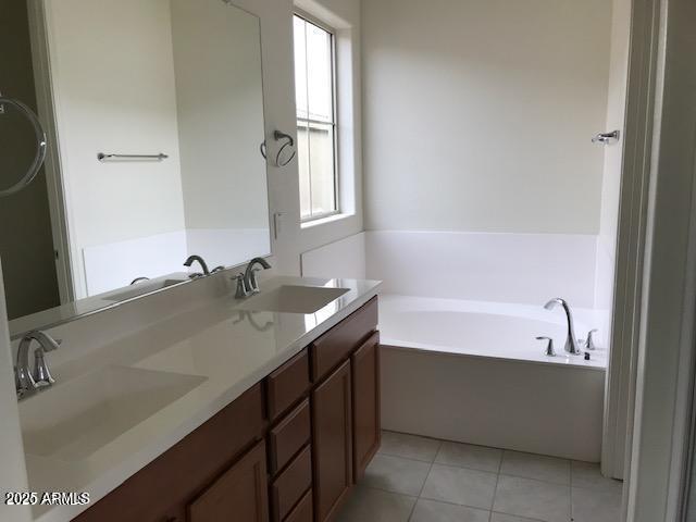 full bathroom featuring tile patterned floors, a garden tub, double vanity, and a sink