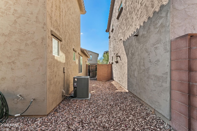 view of side of property featuring central air condition unit, stucco siding, and fence