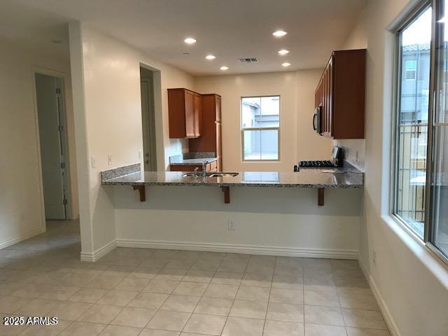 kitchen featuring baseboards, recessed lighting, stove, stone countertops, and a sink