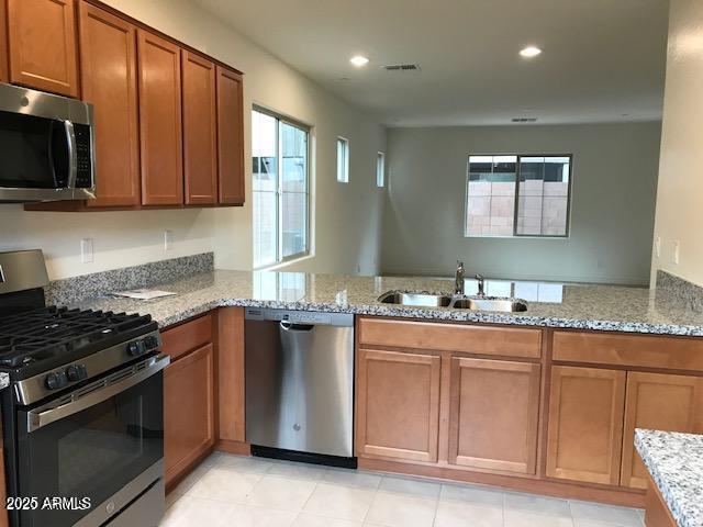 kitchen with a sink, brown cabinetry, light stone countertops, and stainless steel appliances