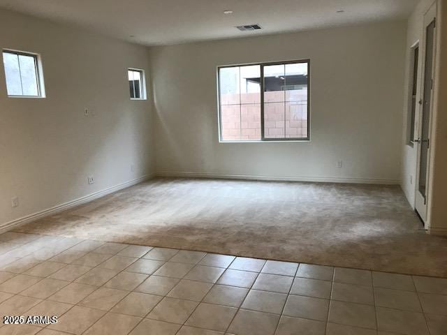 unfurnished room with light tile patterned floors, baseboards, visible vents, and light carpet