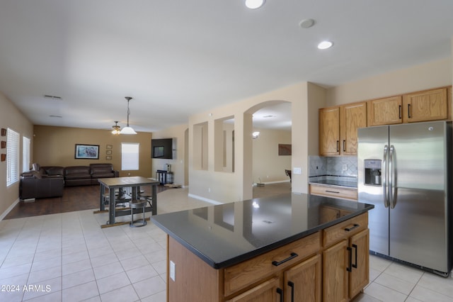 kitchen with hanging light fixtures, light tile patterned flooring, a kitchen island, ceiling fan, and stainless steel refrigerator with ice dispenser