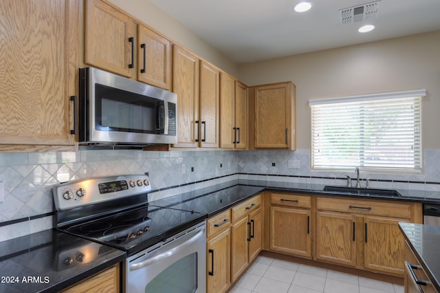 kitchen with dark stone counters, sink, decorative backsplash, stainless steel appliances, and light tile patterned floors